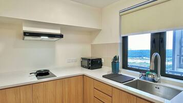 A compact kitchen with a microwave, toaster, and sink. There's a window with a view of the sea.