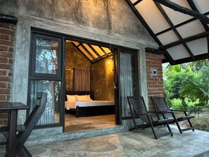 Une chambre avec un lit, une fenêtre et une porte donnant sur un espace extérieur où se trouve une chaise.