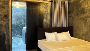 Ein Schlafzimmer mit einem großen Bett, einem Holzkopfende und Blick auf einen Garten durch eine offene Tür.