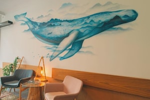 A room with a mural of a whale, two chairs, a small table, and a hanging lamp.