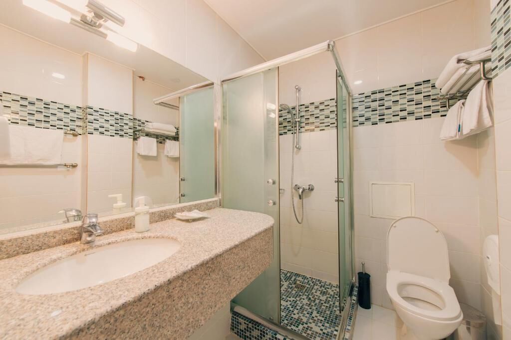 A bathroom with a granite countertop sink, a glass-enclosed shower, and a white toilet.