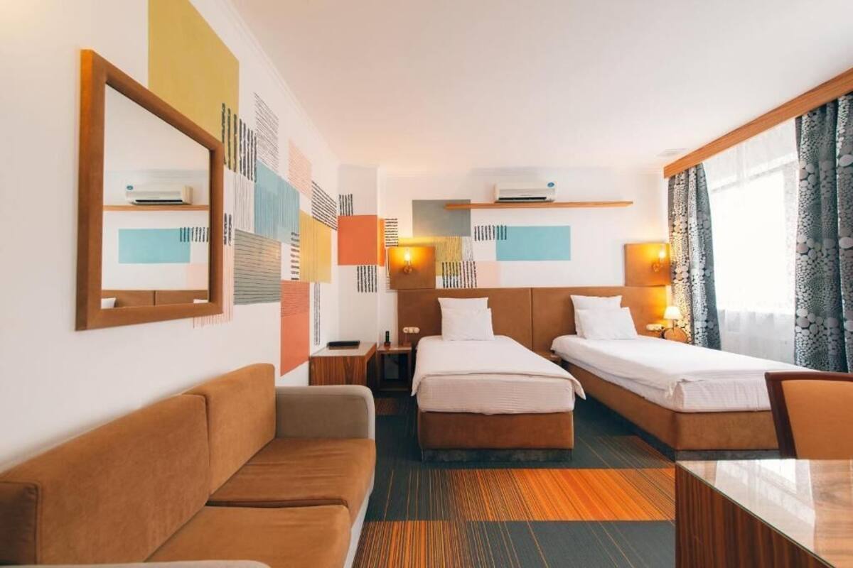 A hotel room with two beds, a sofa, a table, and a mirror.