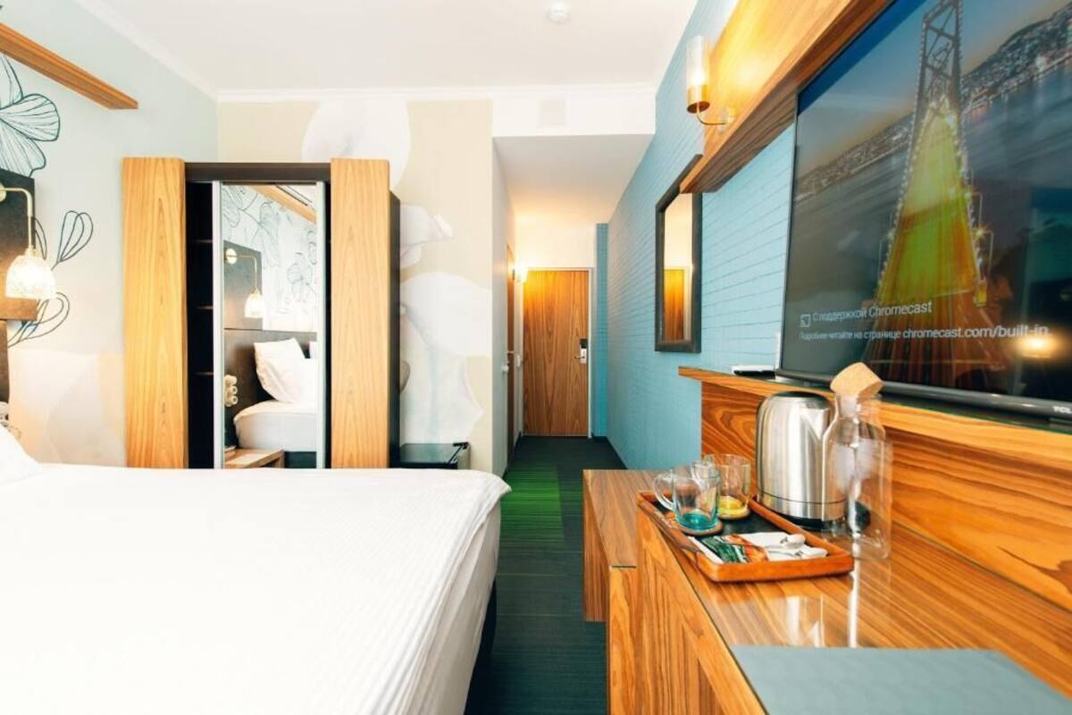 A hotel room with a bed, a wooden desk with a tray of breakfast items, a television, and a large window with a cityscape view.