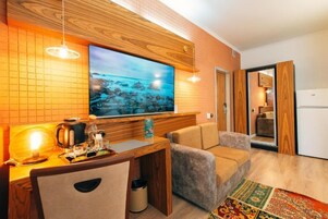 Una sala moderna con un televisor de pantalla plana grande montado en una pared de madera, una pequeña mesa de madera con una tetera y vasos, un sofá y una alfombra colorida.