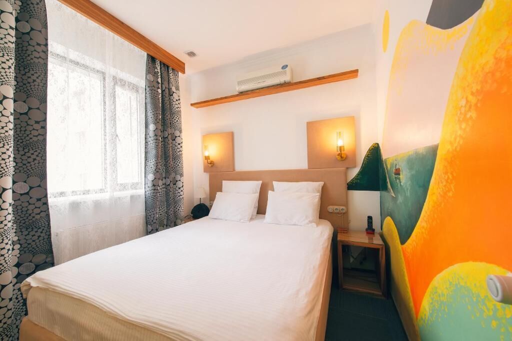 Ein Hotelzimmer mit einem Bett, zwei Nachttischen, einer Wand-Klimaanlage und einem großen abstrakten Gemälde.
