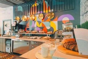 Una cocina moderna con estación de café, electrodomésticos de acero inoxidable y un llamativo diseño abstracto en la pared.