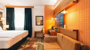 Habitación de hotel con cama, sofá, una mesita de noche con lámpara y un espejo en la pared.