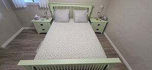 A bed with a patterned bedspread, two bedside tables with lamps, and a window with white curtains. - The Funny Farm (Abbotsford)
