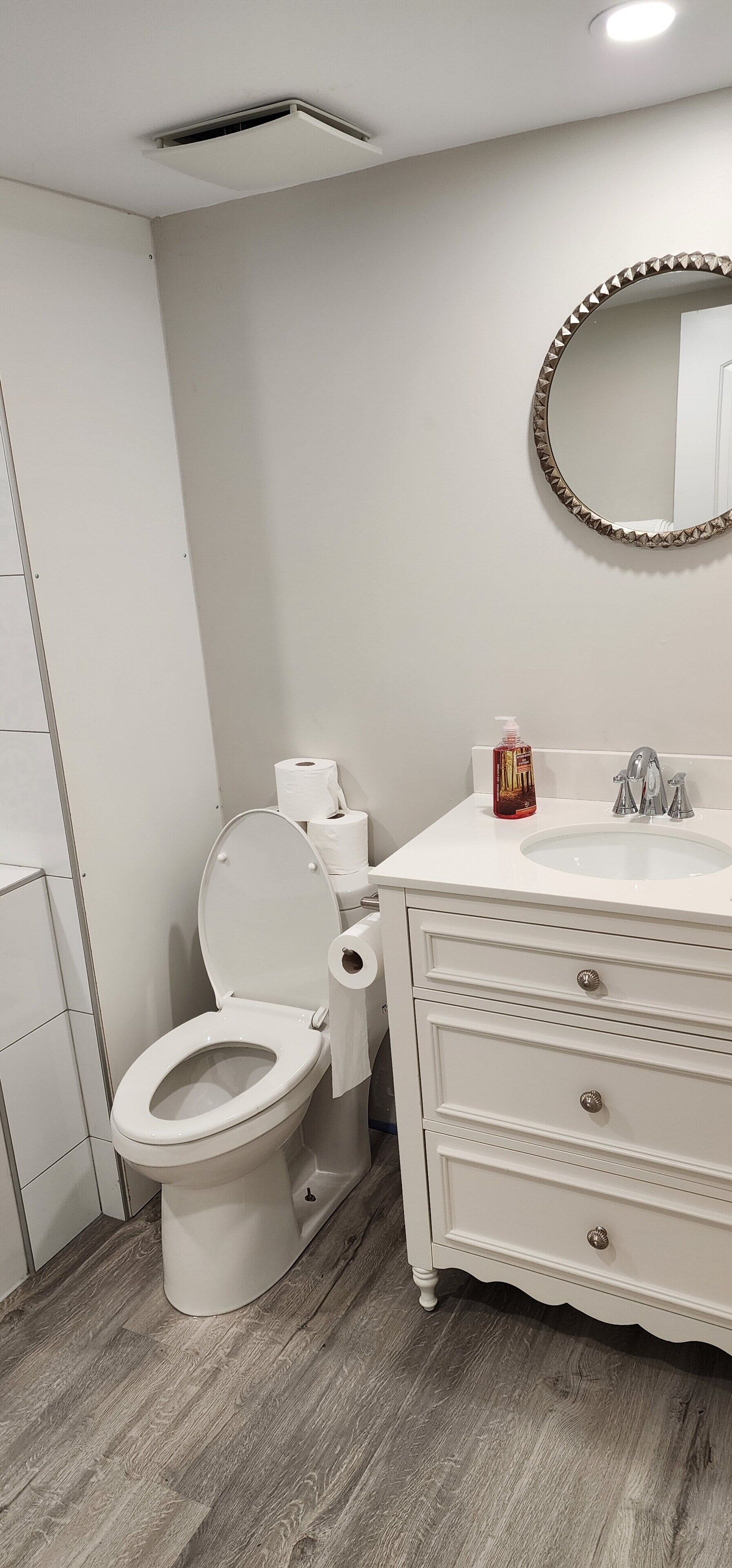 A bathroom with a toilet, sink, mirror, and a roll of toilet paper.