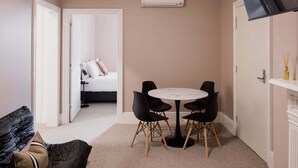 Ein gemütlicher Raum mit rundem Tisch und vier Stühlen, einem Bett im Hintergrund und einer Klimaanlage an der Wand.