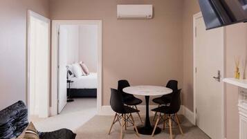 A compact room with a round table and four chairs, a bed in the background, and an air conditioning unit on the wall.
