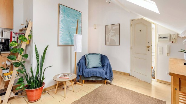 A cozy room with a skylight, a blue chair, a potted plant, and artwork on the walls. - Trendy Loft Heart Of The City! (Lisbon)