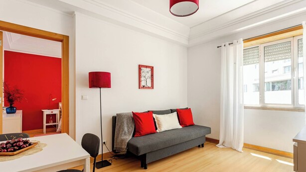 A modern living room with a grey sofa, red cushions, a small table with a bowl of fruit, a floor lamp, and a window with curtains. - Top Location Beautiful Apartment! (Lisbon)