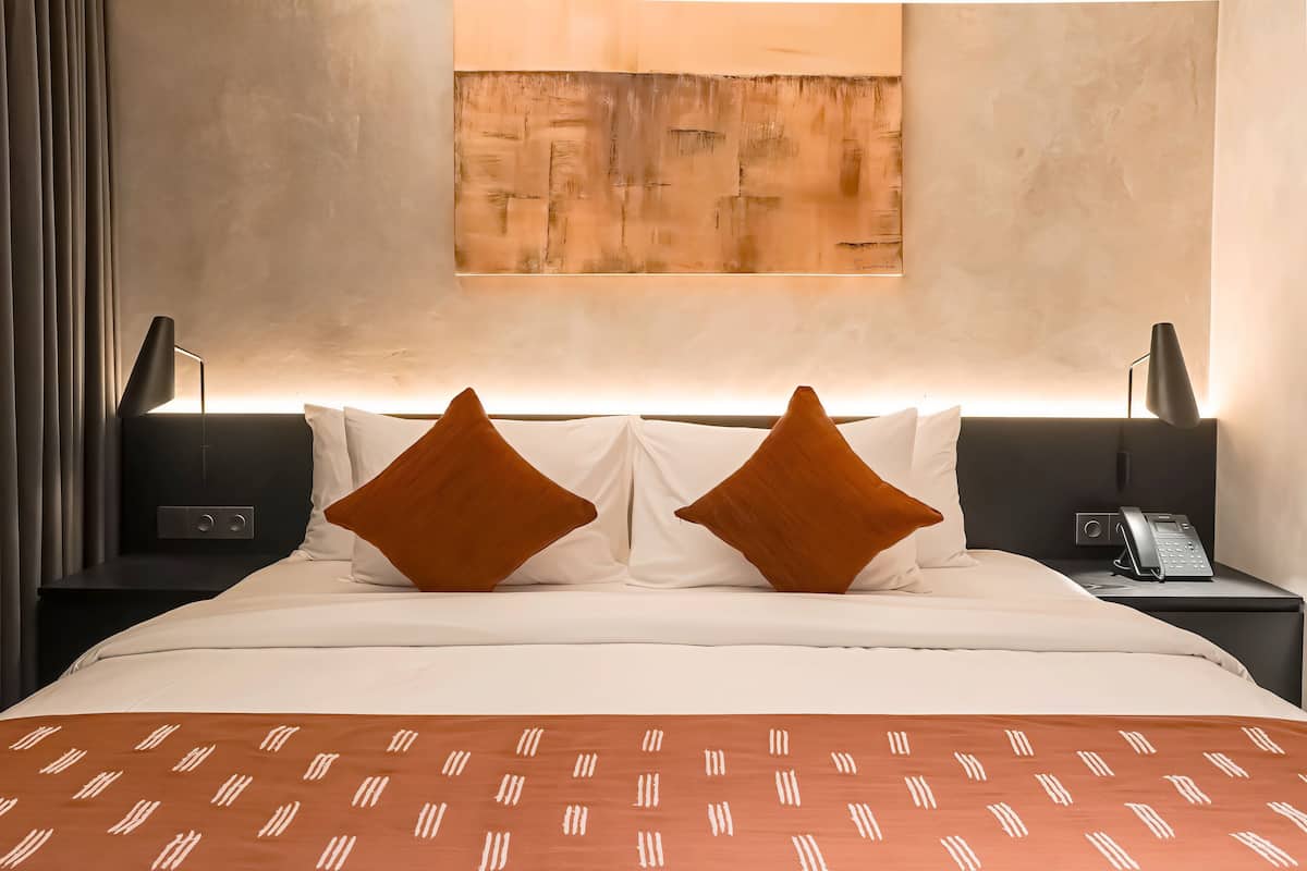 Una camera d'hotel con un letto, due comodini, un telefono e un quadro appeso al muro.