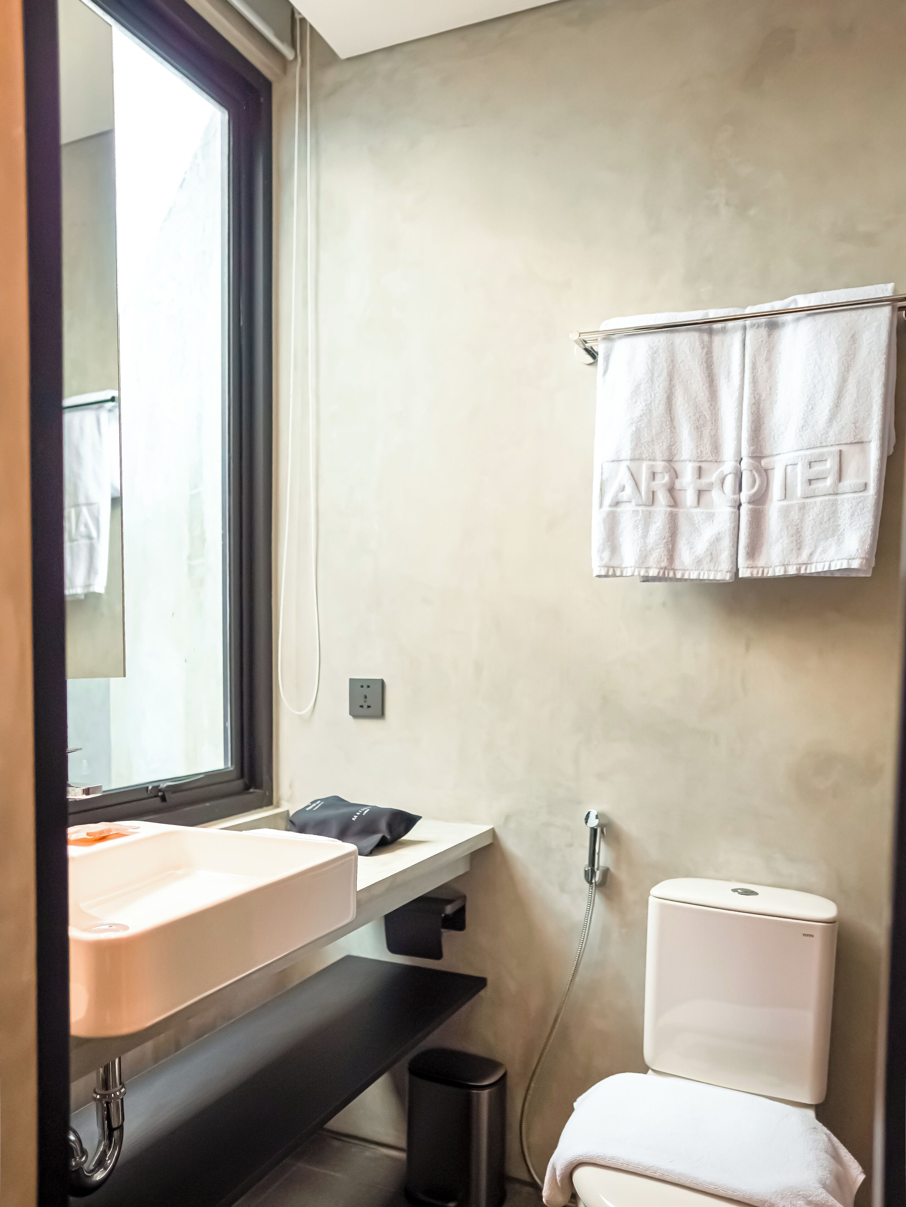 Ein modernes Badezimmer mit großem Fenster, Waschbecken, Toilette und Handtuchhalter mit Handtuch.
