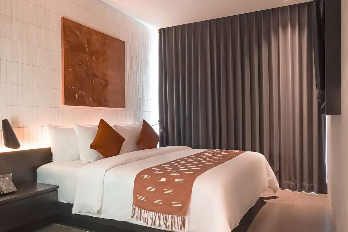 Una camera d'albergo moderna con un letto rifatto, un comodino con una lampada e un'ampia finestra con tende.