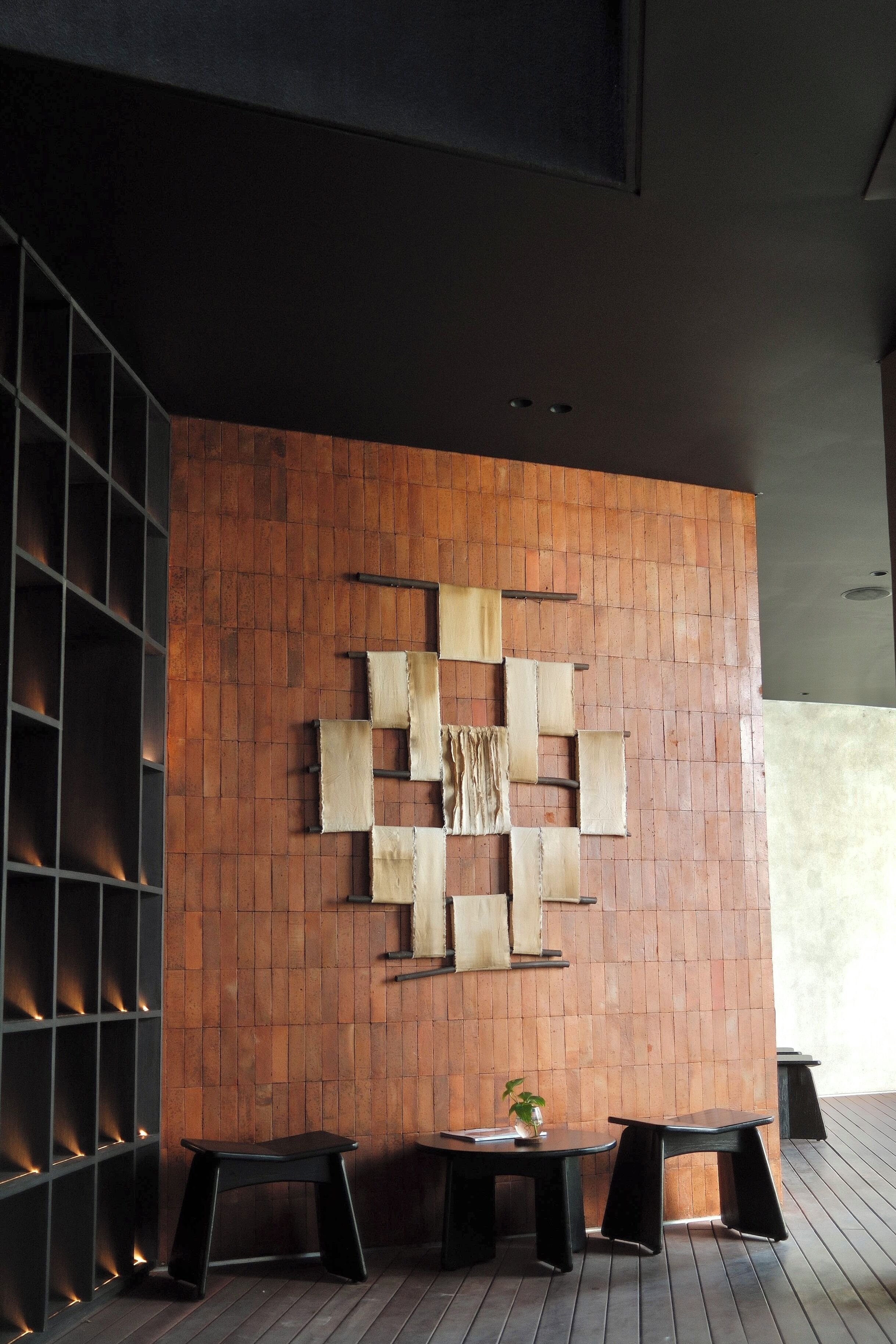 Un interior moderno con una pared de madera, dos taburetes negros y una pequeña mesa con una planta.