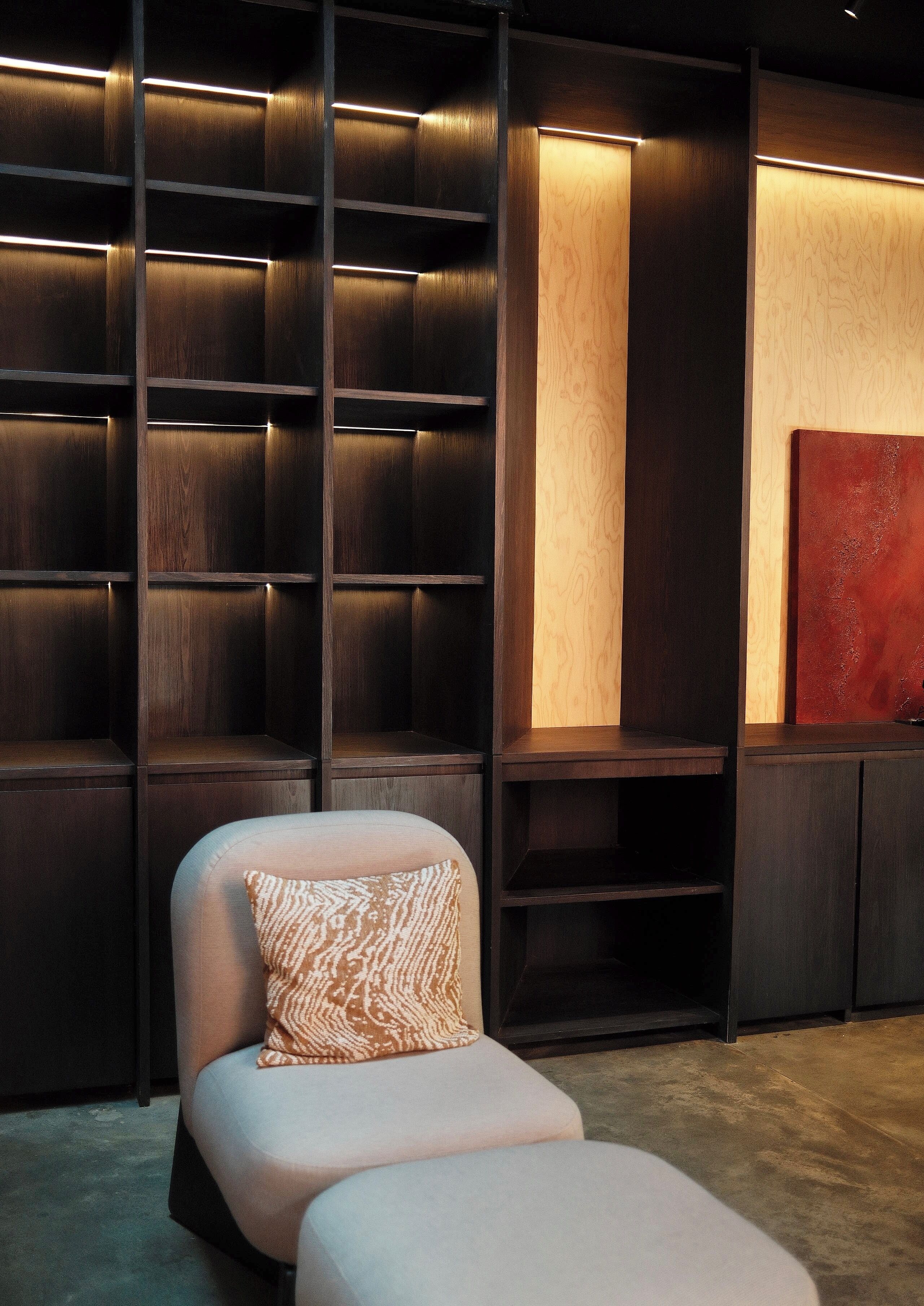 A modern room with a built-in shelving unit, a cushioned seating area, and a large abstract painting on the wall.