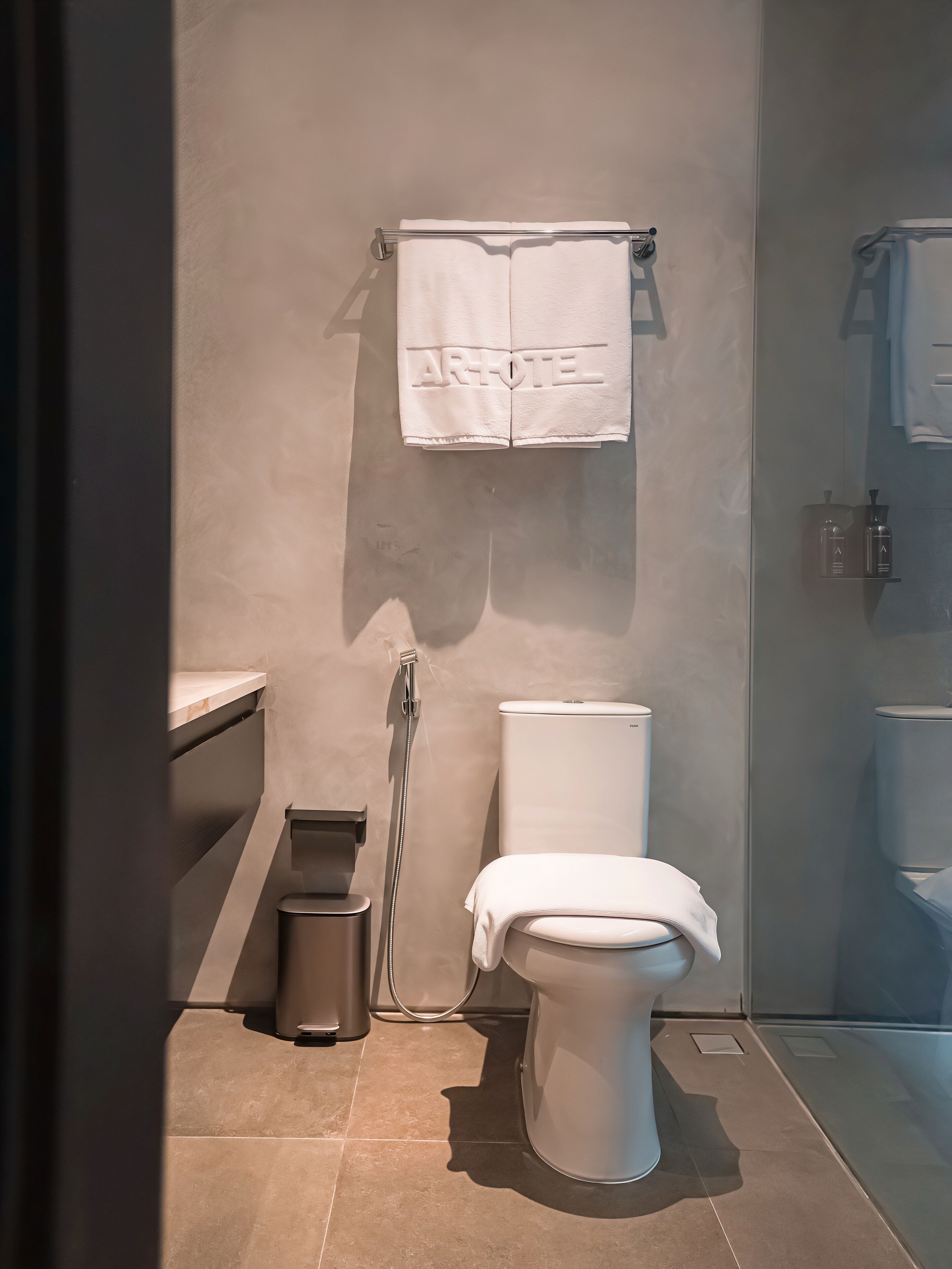 Un baño moderno con inodoro, ducha y toallero con una toalla colgada.