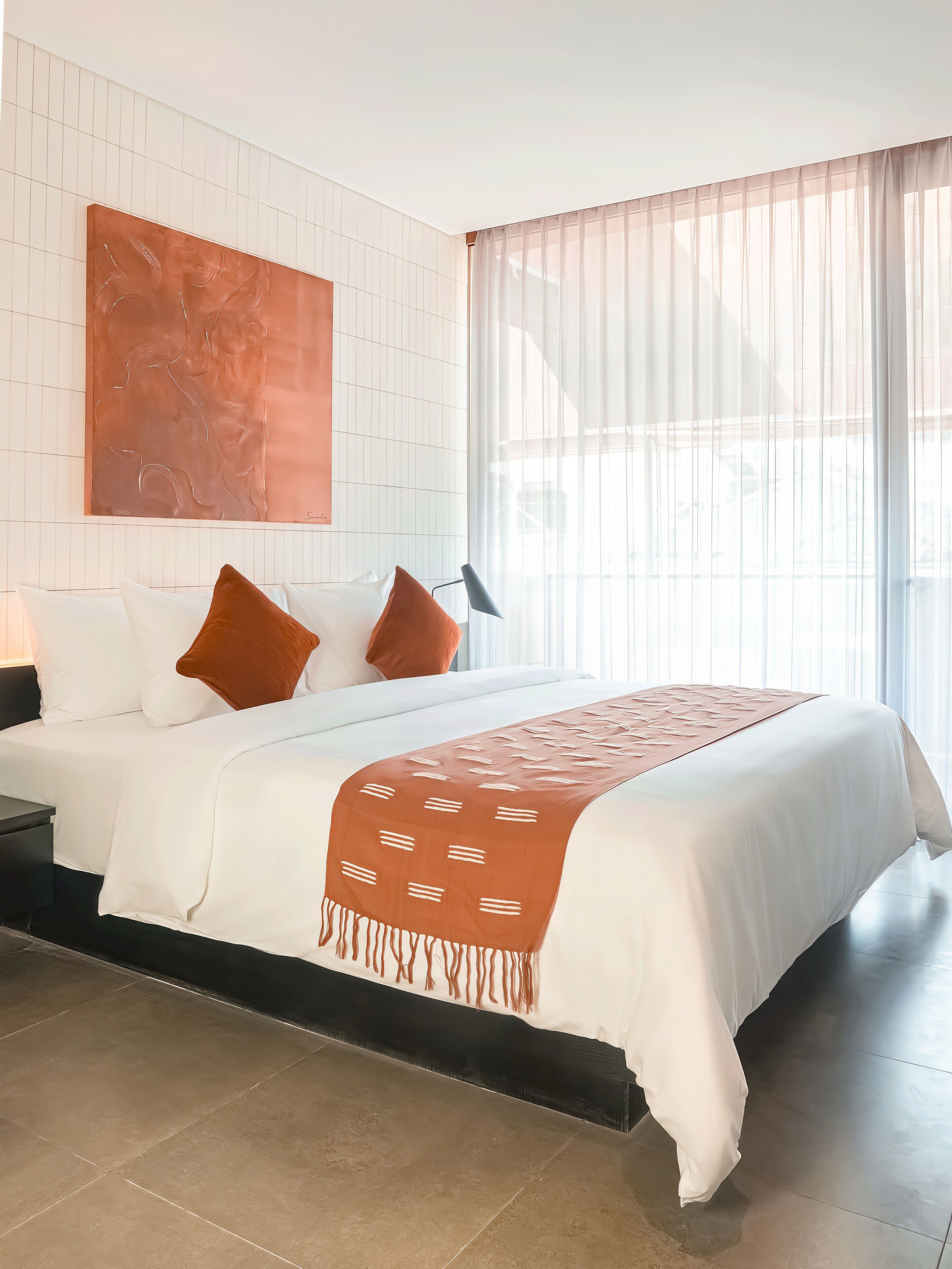 A modern hotel room with a large bed, white bedding, a brown throw blanket, and a large abstract painting on the wall.