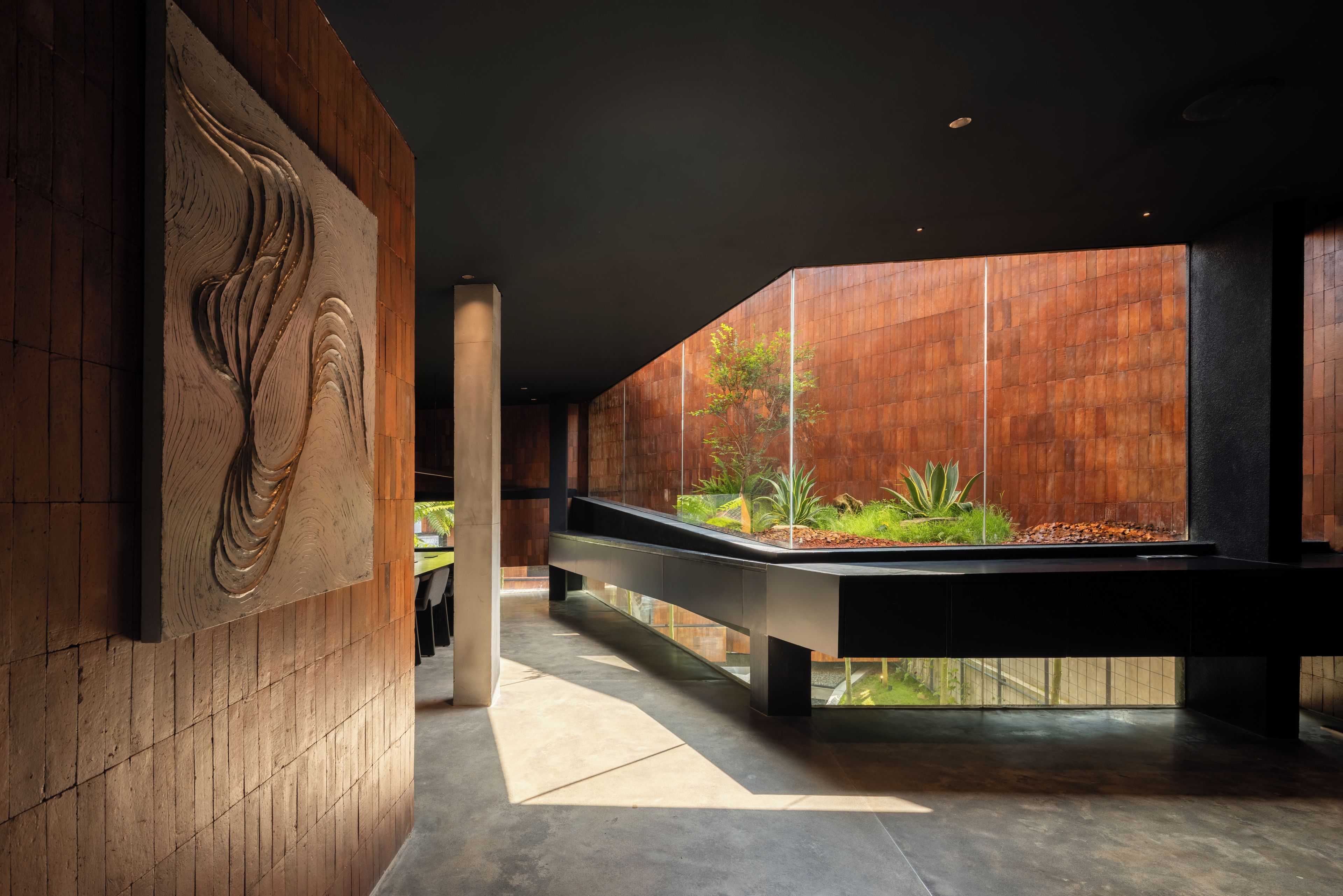 Un interior moderno con un largo pasillo, paneles de madera, un macetero central con plantas y una escultura grande montada en la pared.