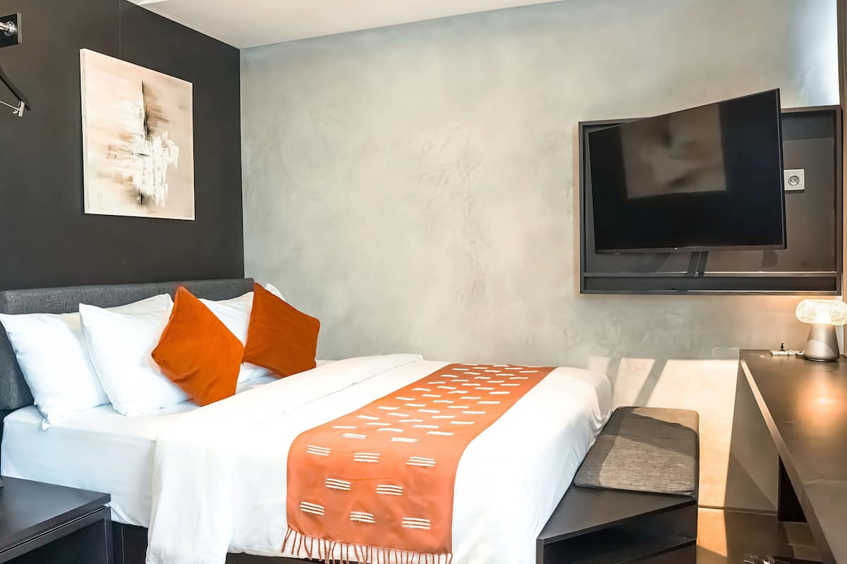 Camera da letto moderna con un letto, una TV a schermo piatto montata a parete e un comodino con una lampada.