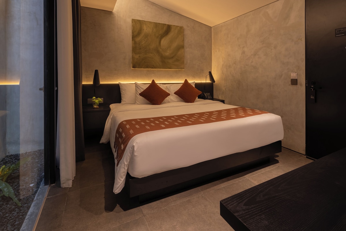A modern hotel room with a large bed, bedside tables, a wall-mounted artwork, and a door with a lock.
