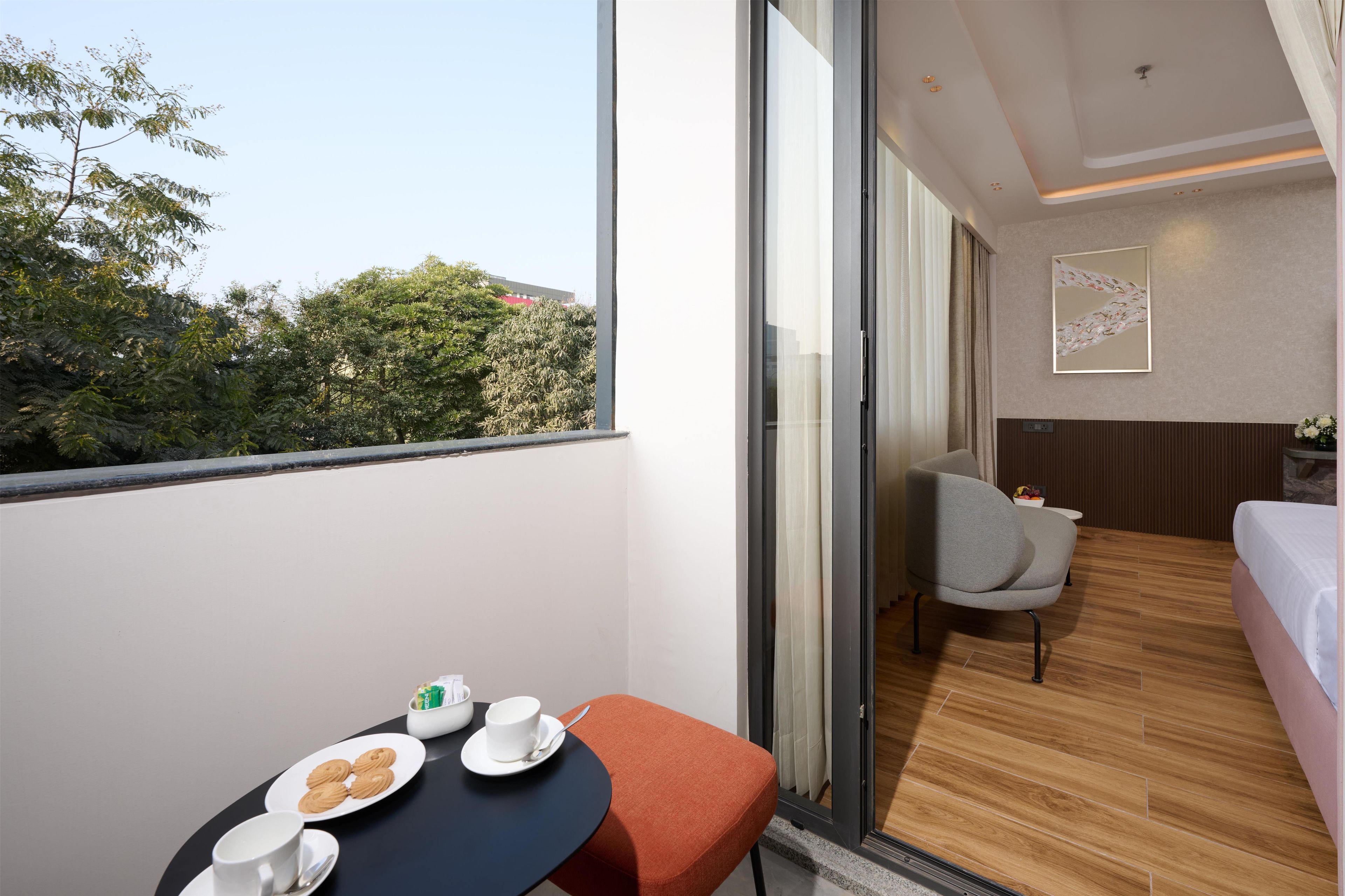 A modern hotel room with a balcony, a dining area with a table and chairs, and a view of the cityscape.