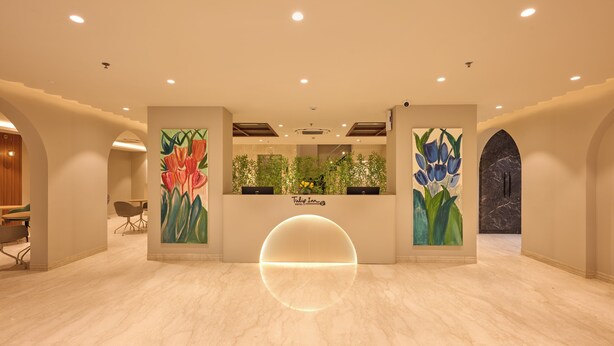Ein Hotel-Empfangsbereich mit Marmorboden, einer zentralen Rezeption und zwei großen Wandgemälden mit floralen Motiven.