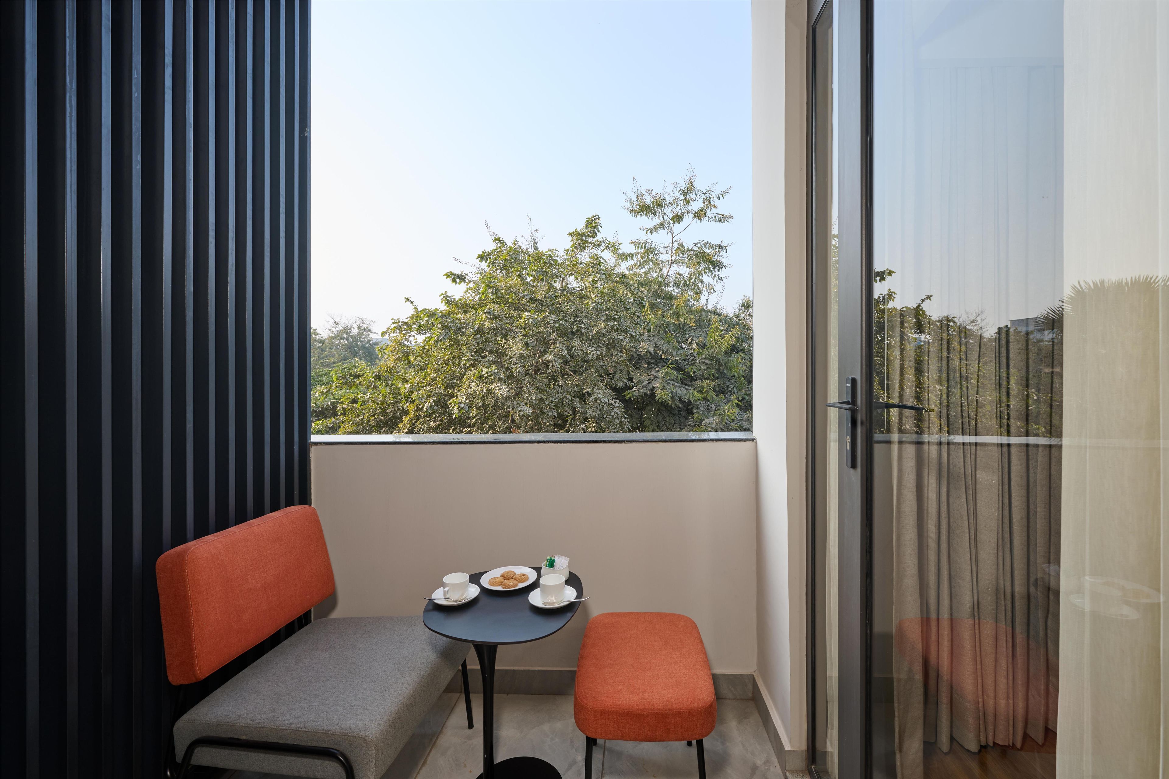 Un balcon avec un canapé, une petite table avec des tasses et des pâtisseries, et une vue sur les arbres.