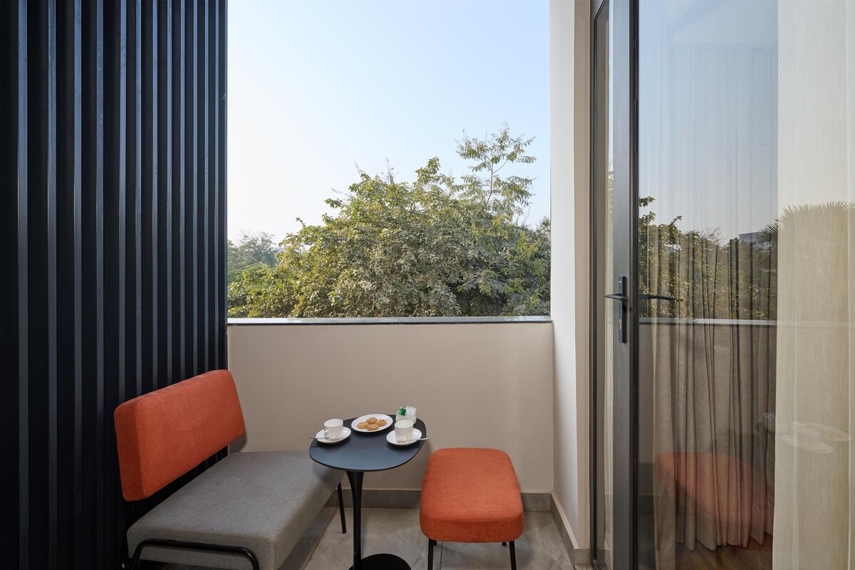 A balcony with a sofa, a small table with cups and pastries, and a view of trees.