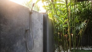 A concrete shower enclosure with a handheld showerhead, surrounded by lush greenery. - Island’s Gift – Private Design House for 2 Near Sunset Beach (Koh Phangan)