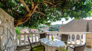 A balcony with a table and chairs, a stone wall, and a view of buildings and trees. - Apartments Katica's Place - One Bedroom Apartment With Terrace and City View (Blato)