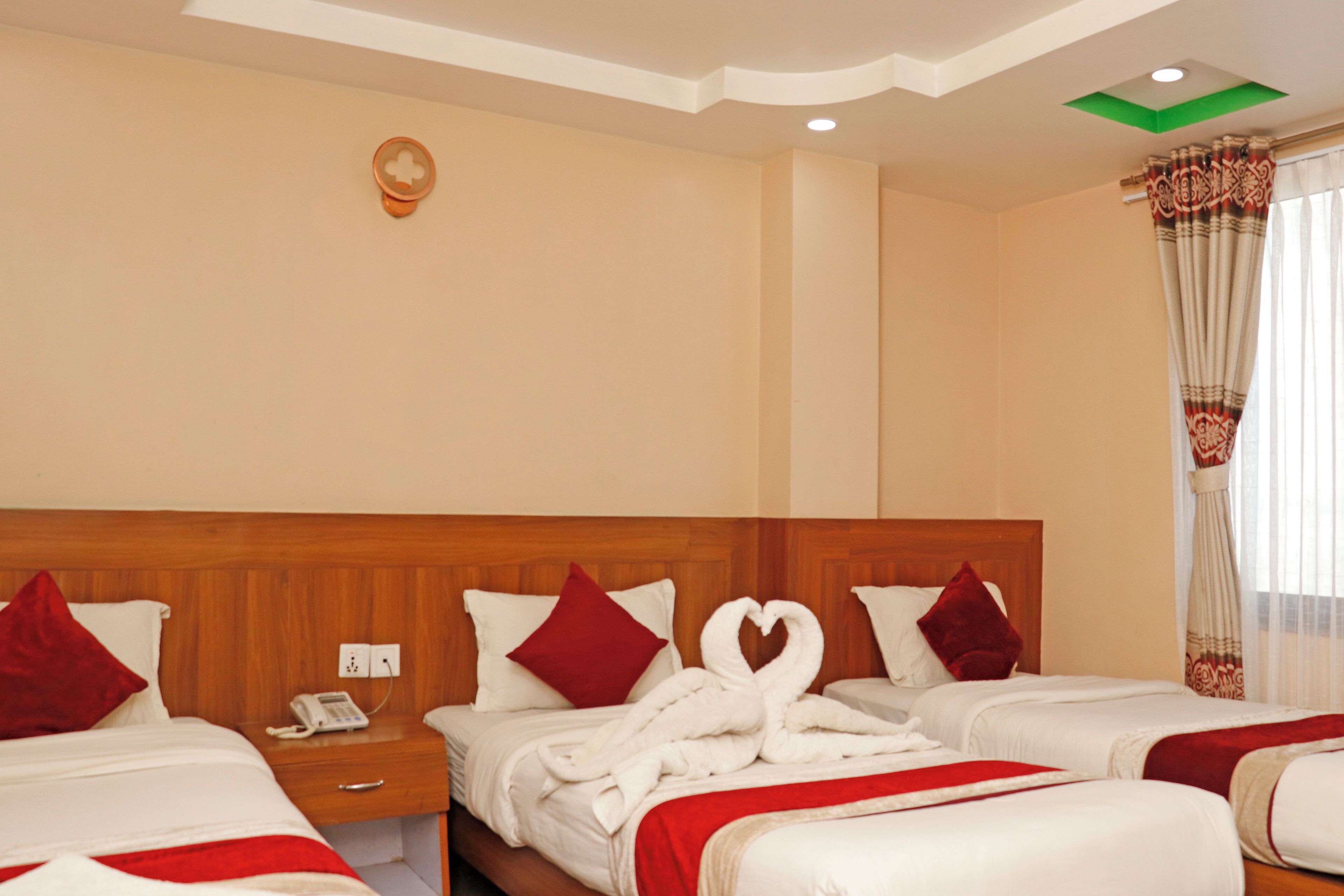 A hotel room with three beds, a wooden headboard, a telephone on the nightstand, and a wall-mounted light fixture.