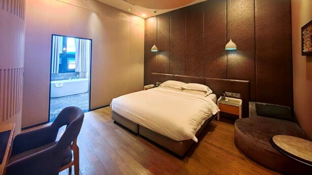 Habitación de hotel moderna con una cama grande, un escritorio y una silla. Se ve el exterior a través de un ventanal amplio.
