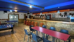 Une salle de billard équipée d’une table de billard, de plusieurs tabourets et d’une longue table rouge.