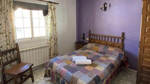 Une chambre à coucher avec un lit en bois, une chaise, une fenêtre avec des rideaux, un radiateur et un luminaire fixé au mur.