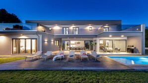 Een modern huis met een zwembad, buitenmeubilair en een goed verlicht terras.