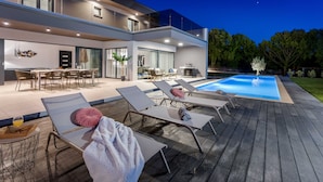 Een modern huis met een zwembad, buitenmeubels en een eethoek.