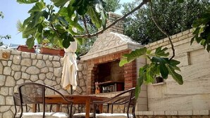 Un'area salotto esterna con pareti in pietra, un forno a mattoni e sedie in metallo.