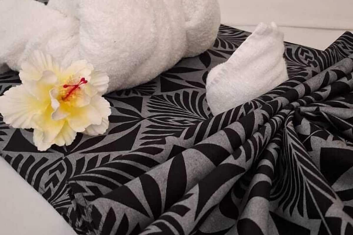 Una cama con una colcha de diseño blanco y negro, dos toallas blancas formando cisnes, y una flor de hibisco amarilla.