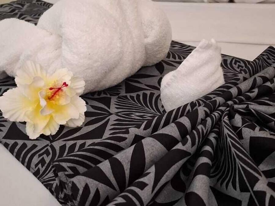 Una cama con una colcha de diseño blanco y negro, dos toallas blancas formando cisnes, y una flor de hibisco amarilla.