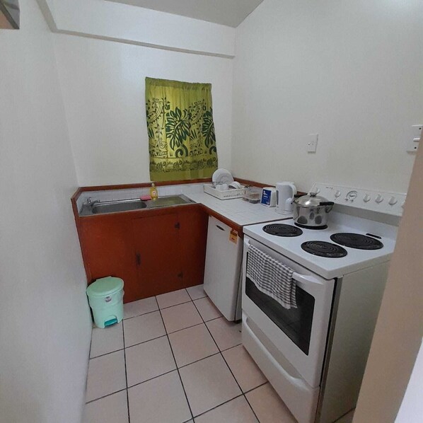 A compact kitchen with a stove, sink, and a small trash bin. - Samoa Holiday Hotel (Apia)