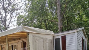 Ein Mobilheim mit überdachter Veranda und einer separaten Blockhütte.