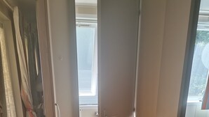 Ein Zimmer mit einem Holzschrank, einer zur Toilette führenden Tür und einem Fenster mit Blick nach draußen.