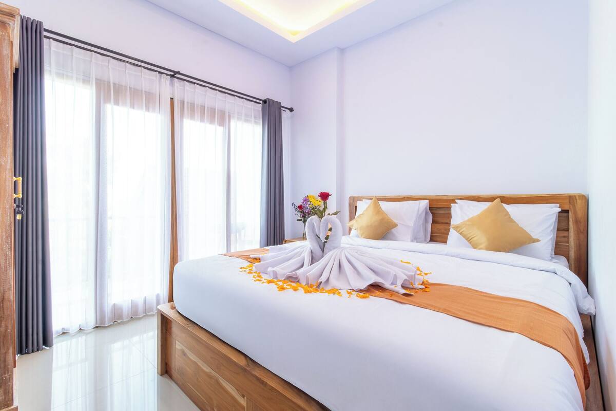 A neatly made bed with a wooden headboard, white bedding, and a decorative arrangement of towels and flowers.