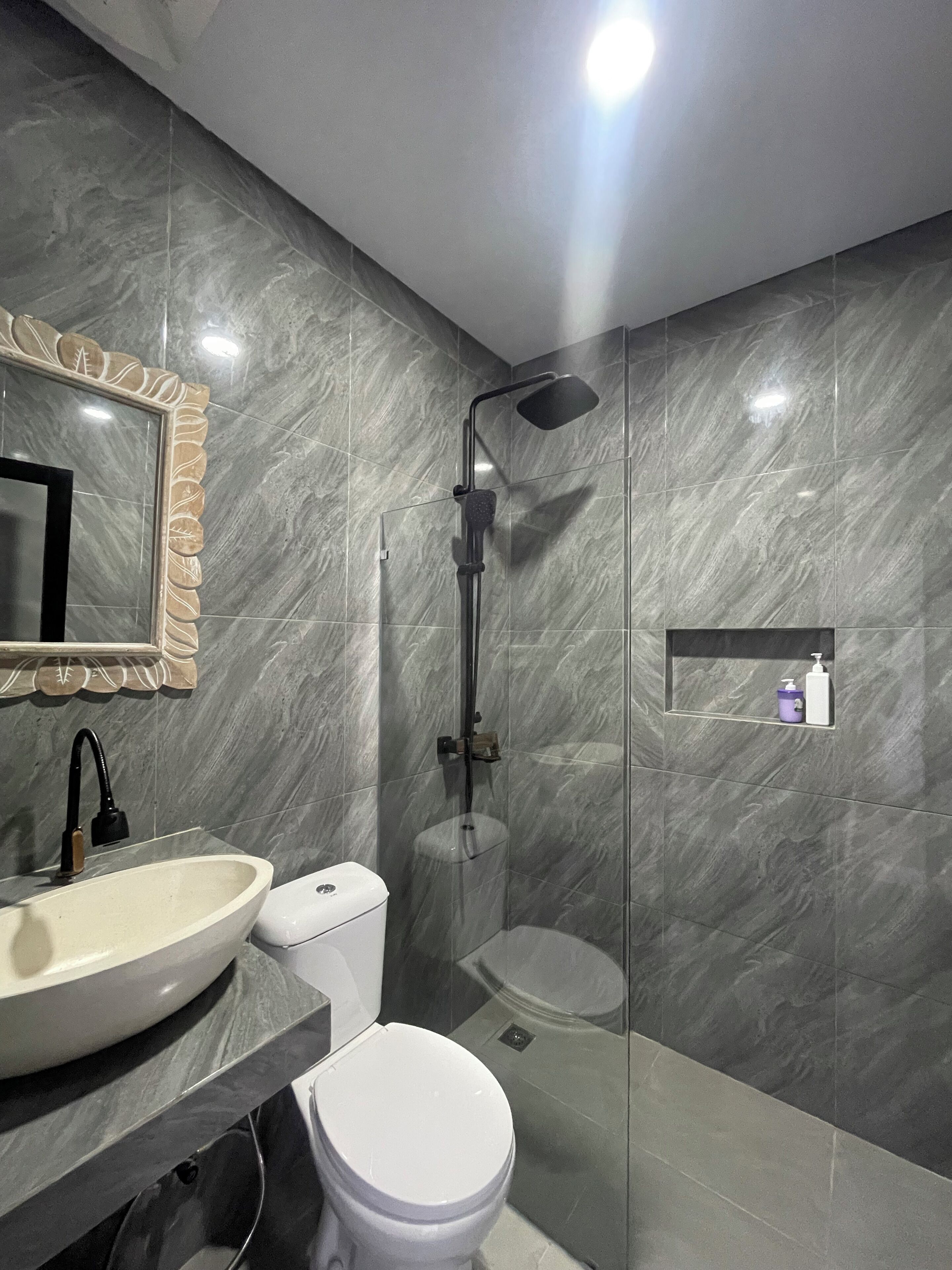 A modern bathroom with a marble wall, a sink, toilet, and a glass-enclosed shower.