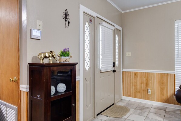 A hallway with a wooden door, a thermostat, a welcome sign, and a decorative shelf.