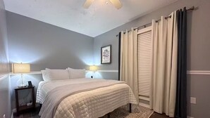 A bedroom with a bed, nightstands, a lamp, a ceiling fan, and a window with curtains.