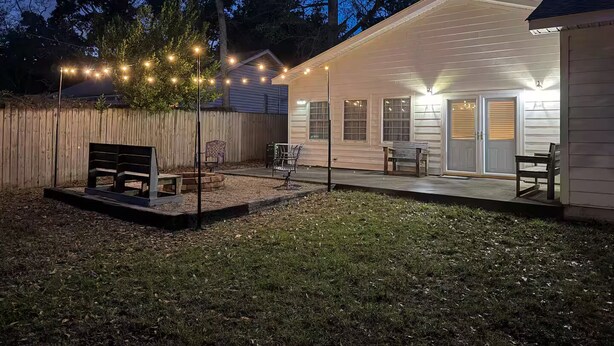 A backyard with a wooden deck, outdoor furniture, and string lights.